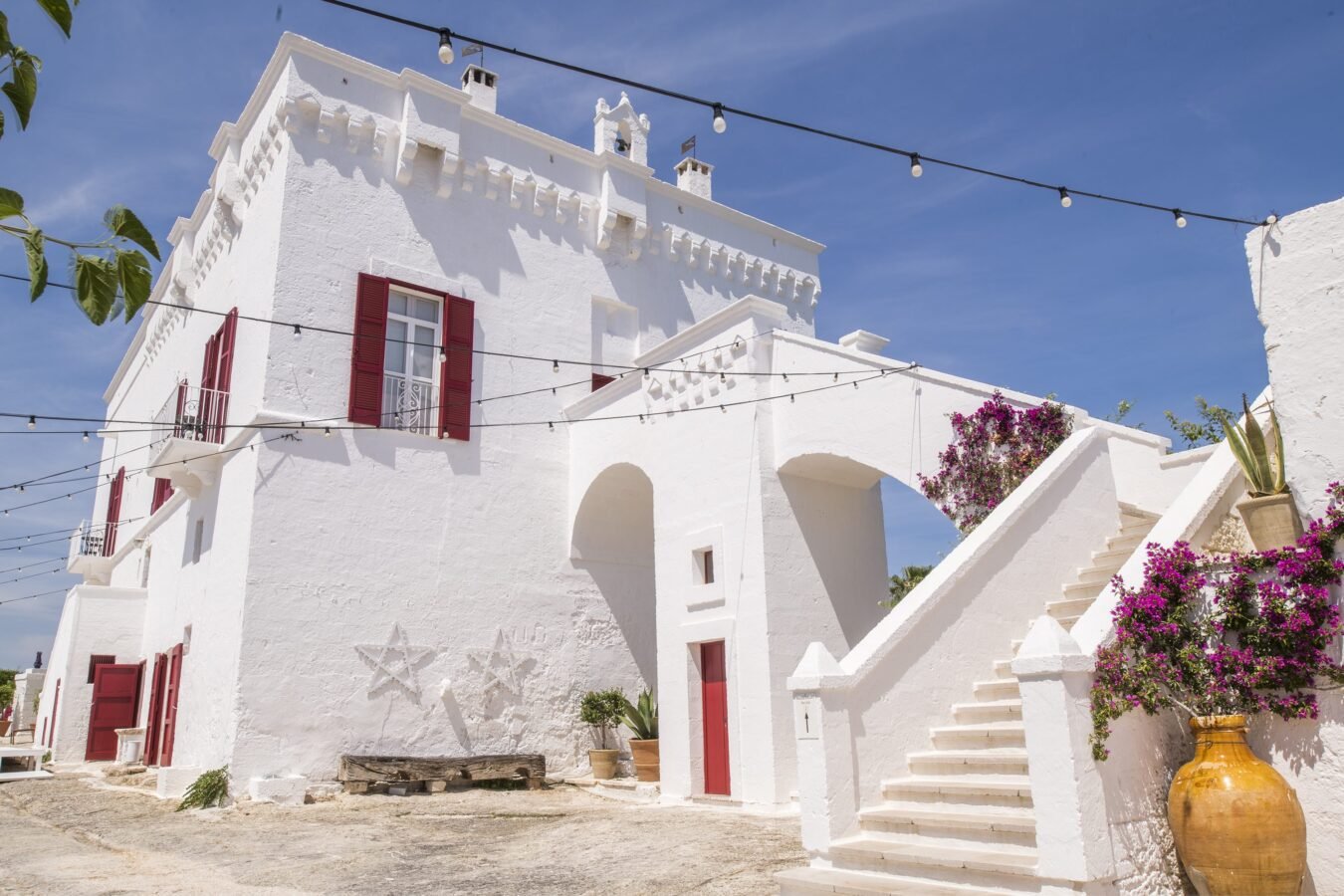 White washed Puglia masseria farmhouse luxury hotel with flowers and under blue sky