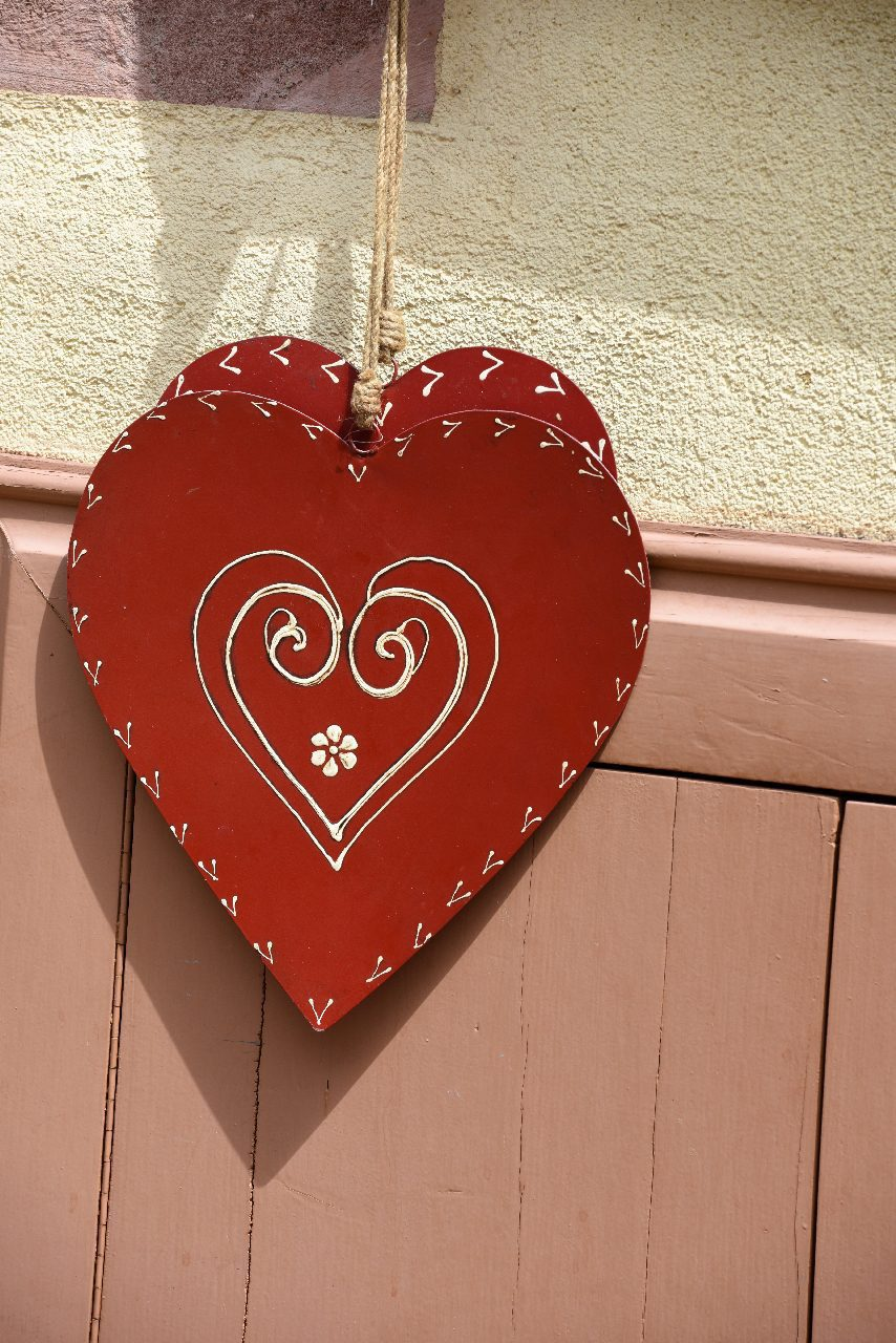 A red heart with decorative swirls hangs on a village wall on the Alsace wine route in France